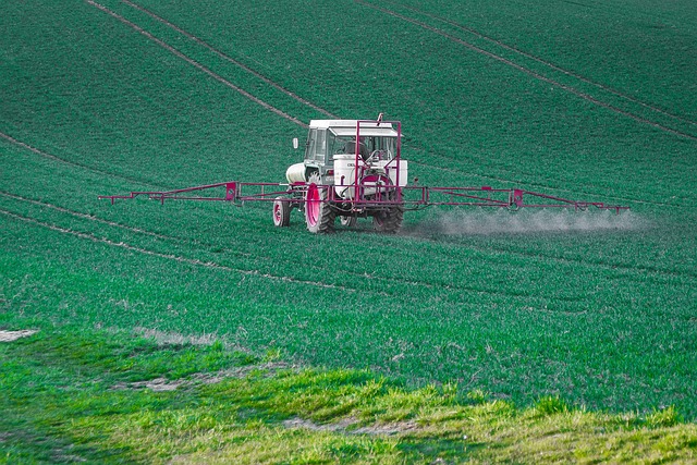 A farmer in a red tractor spraying a field with glyphosate to control weeds